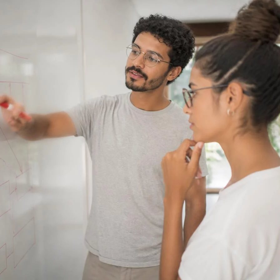 Duas participantes de pé junto ao quadro branco, desenhando as partes de um argumento